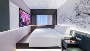 A modern hotel room with a large bed, a flat-screen TV, a desk with a computer, and a wall with sketches and text. - CitiGO Hotel Ouzhuang (Guangzhou)
