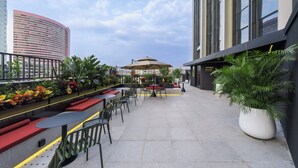 An outdoor seating area with tables and chairs, surrounded by potted plants and a large umbrella. - CitiGO Hotel Ouzhuang (Guangzhou)