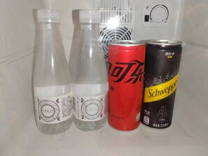 Tres botellas y dos latas de bebidas sobre una estantería.