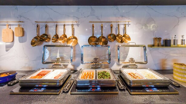 Estaciones de buffet con diversas opciones de comida, una pared de mármol y macetas colgantes.