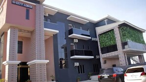 A modern building with a sign reading "CITY LODGE". It features multiple balconies, a flat roof, and a mix of brick and glass facades. - V City Lodge Hotel and Suites (Abuja)