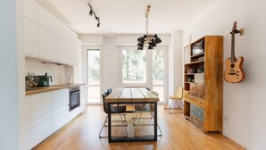 Una cuina moderna amb taula de fusta, armaris blancs i una guitarra penjada a la paret.
