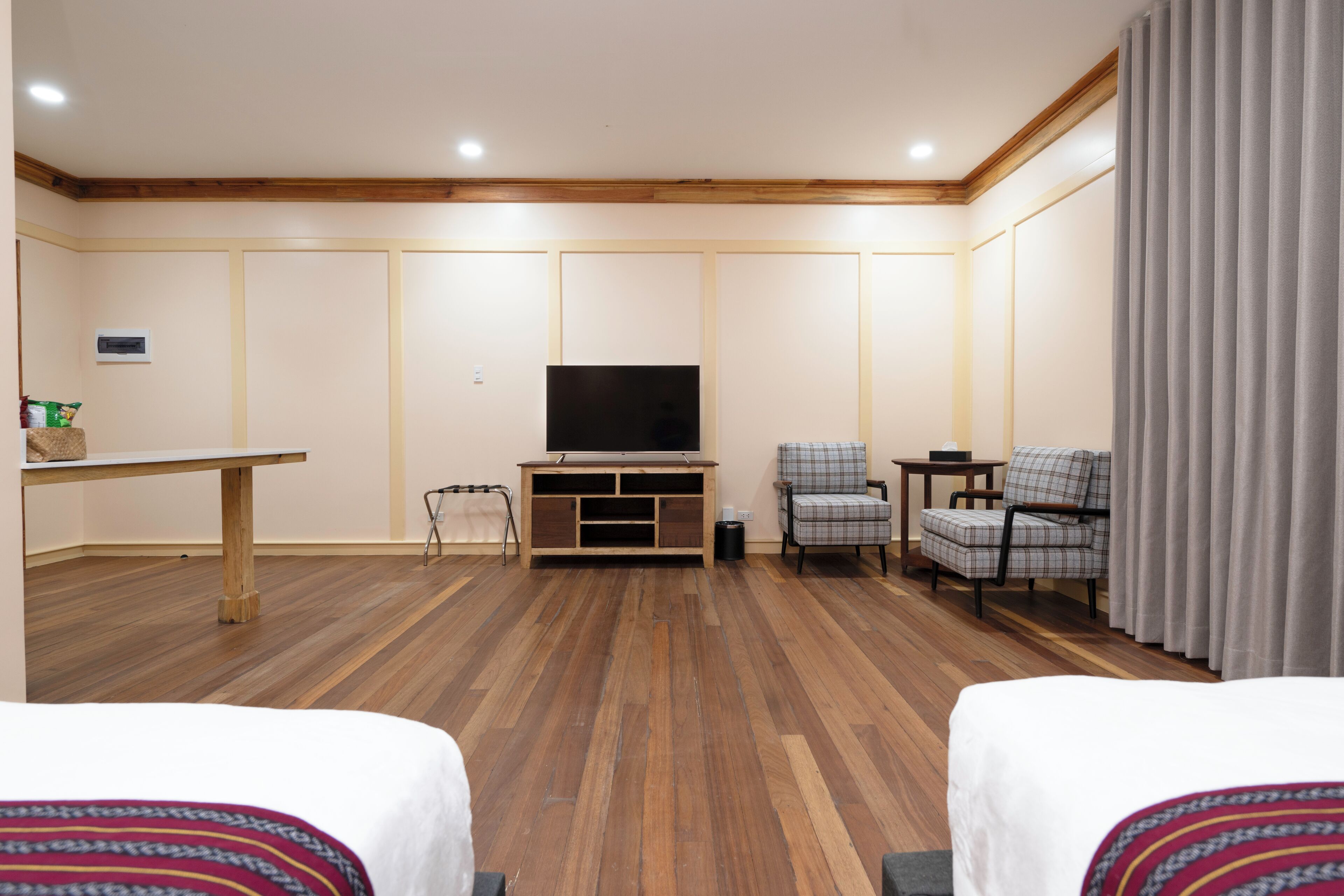 Een hotelkamer met twee bedden, een televisie, een tafeltje, een stoel en een gordijn.