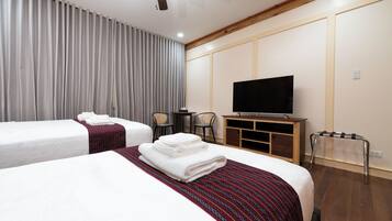 Ett hotellrum med två sängar, en TV, ett skrivbord och en takfläkt.
