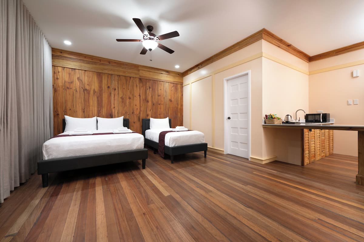 Quarto com duas camas, um ventilador de teto em madeira e uma cozinha compacta com micro-ondas.