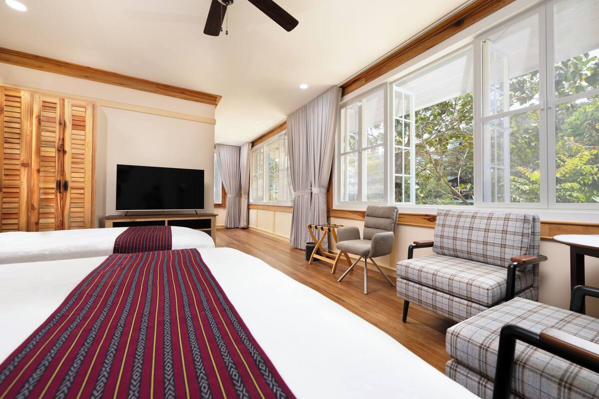 Quarto de hotel com duas camas, televisão, escrivaninha e uma cadeira.