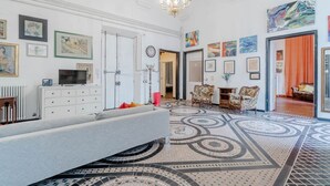 Uma sala de estar espaçosa com um sofá grande, um candelabro e um chão estampado.