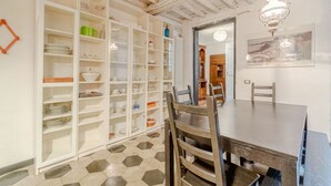 Uma sala de jantar com mesa e cadeiras de madeira, um armário branco com portas de vidro e um chão com padrão hexagonal.