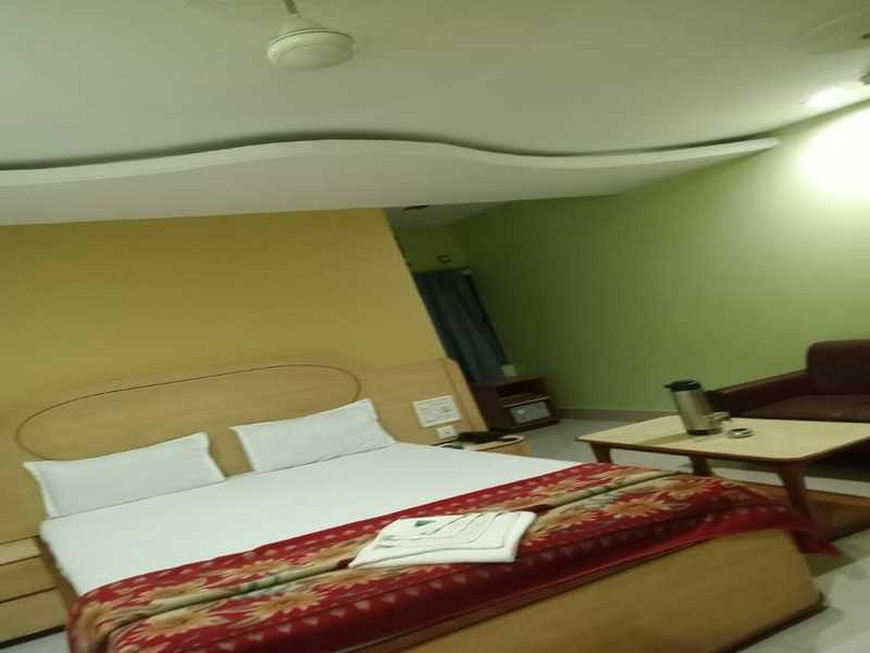 A hotel room with a bed, a bedside table, a chair, and a small table with a cup and saucer.