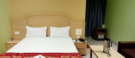 A hotel room with a bed, a desk, a chair, a nightstand, a telephone, and a coffee maker.