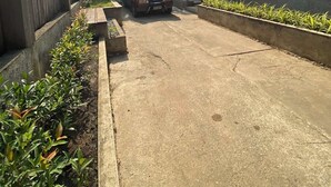Una calle residencial con un coche estacionado, casas de paredes blancas y una valla de madera a la izquierda.