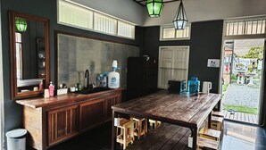 Una cocina con una isla de madera, un lavamanos y un refrigerador. Hay taburetes alrededor de la isla y un dispensador de agua grande.