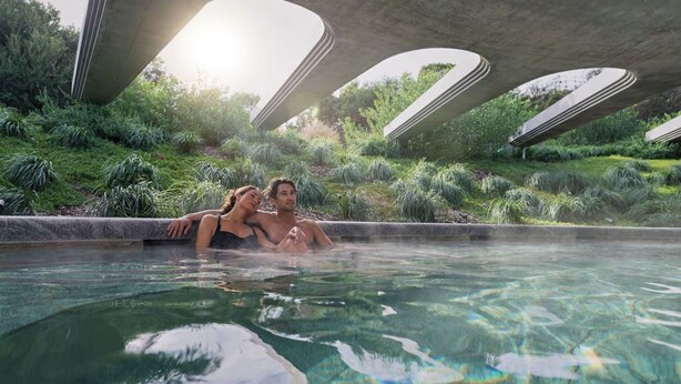 A couple relaxing in a clear pool with a unique architectural structure overhead. - The Sanctuary at Alba Thermal Springs & Spa (Fingal)
