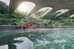 A couple relaxing in a clear pool with a unique architectural structure overhead. - The Sanctuary at Alba Thermal Springs & Spa (Fingal)