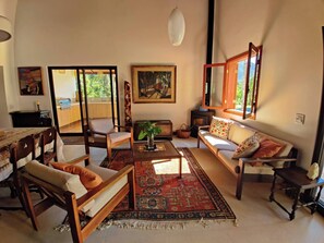 Relax in this spacious living room with a sofa set, armchairs, and a coffee table, surrounded by wall art and a vibrant rug.