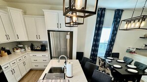 Una cocina moderna con armarios blancos, una isla central con pileta y un comedor con mesa y sillas.