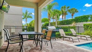 A covered outdoor area with a pool, a grill, and lounge chairs.