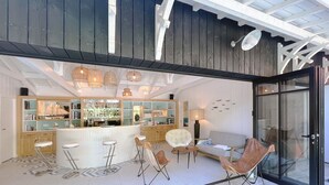 A modern kitchen with a bar area, seating, and a glass door leading outside. - Bassin front villa with private beach access, heated pool - 14 pers (Andernos-les-Bains)