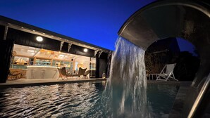 An outdoor pool area with a waterfall feature, a bar with stools, and a covered seating area. - Bassin front villa with private beach access, heated pool - 14 pers (Andernos-les-Bains)