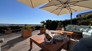 A wooden deck with outdoor furniture, a table with a bottle and glasses, and a view of the sea and pier. - Bassin front villa with private beach access, heated pool - 14 pers (Andernos-les-Bains)