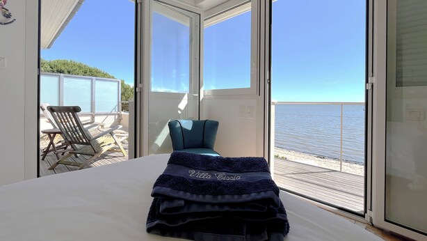 A room with a bed, a blue chair, and a view of the sea through large sliding doors. - Bassin front villa with private beach access, heated pool - 14 pers (Andernos-les-Bains)