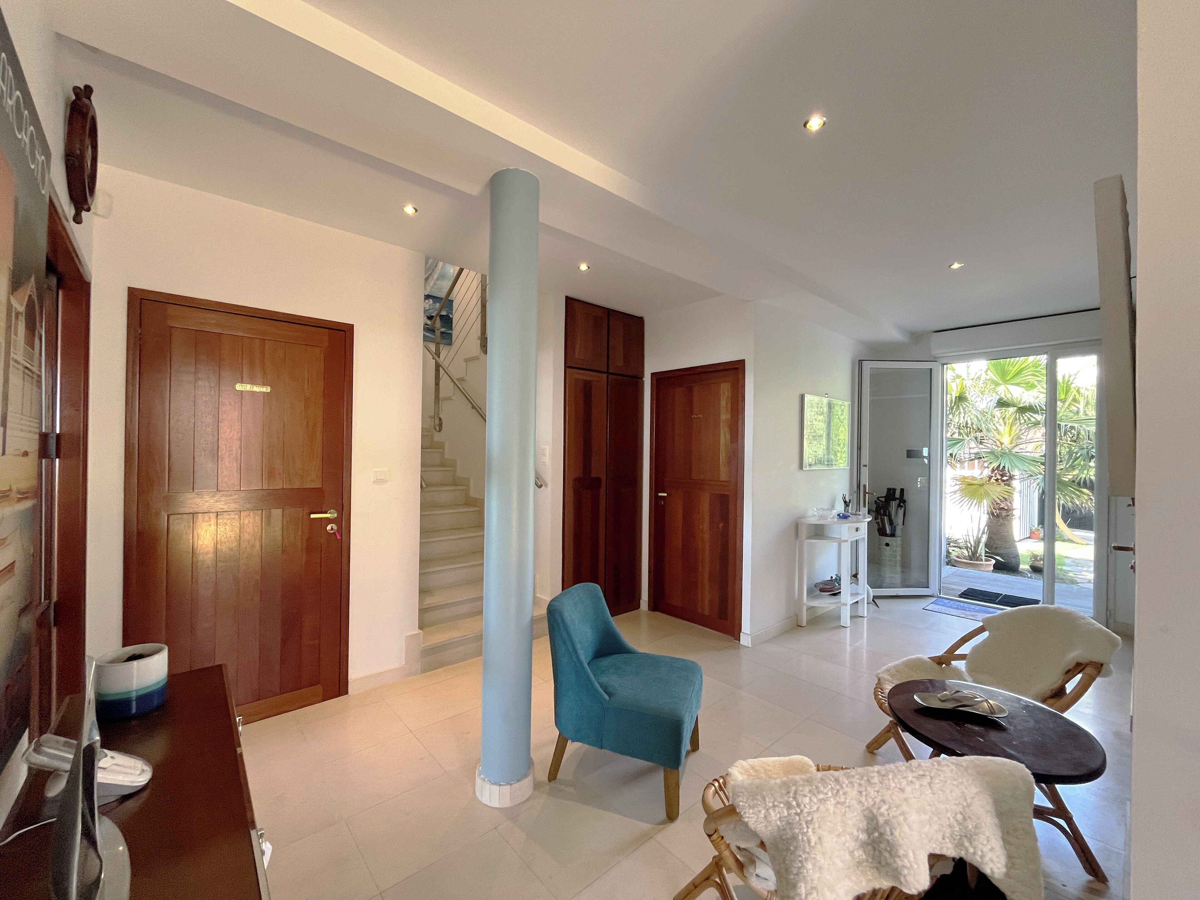 A spacious living area with a blue armchair, a dining table, and a staircase leading to another level.