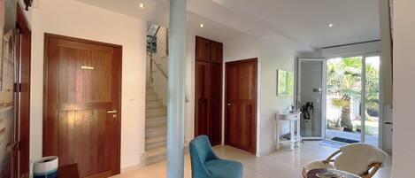 A spacious living area with a blue armchair, a dining table, and a staircase leading to another level.