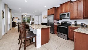 A modern kitchen with wooden cabinets, stainless steel appliances, and a granite countertop island. - Charming Home near Disney: Theme Rooms, Foosball & Waterpark - 370LA (Kissimmee)