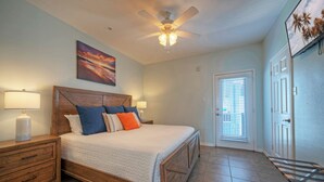 A bedroom with a wooden bed, two bedside tables with lamps, a ceiling fan, and a door with blinds.