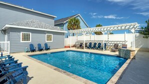 A swimming pool with blue water, surrounded by blue chairs and a white pergola.