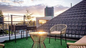 A rooftop patio with a table and chairs, a grill, and a view of the sunset.