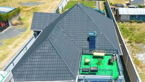 A rooftop terrace with a green floor, metal railings, and a blue water heater.
