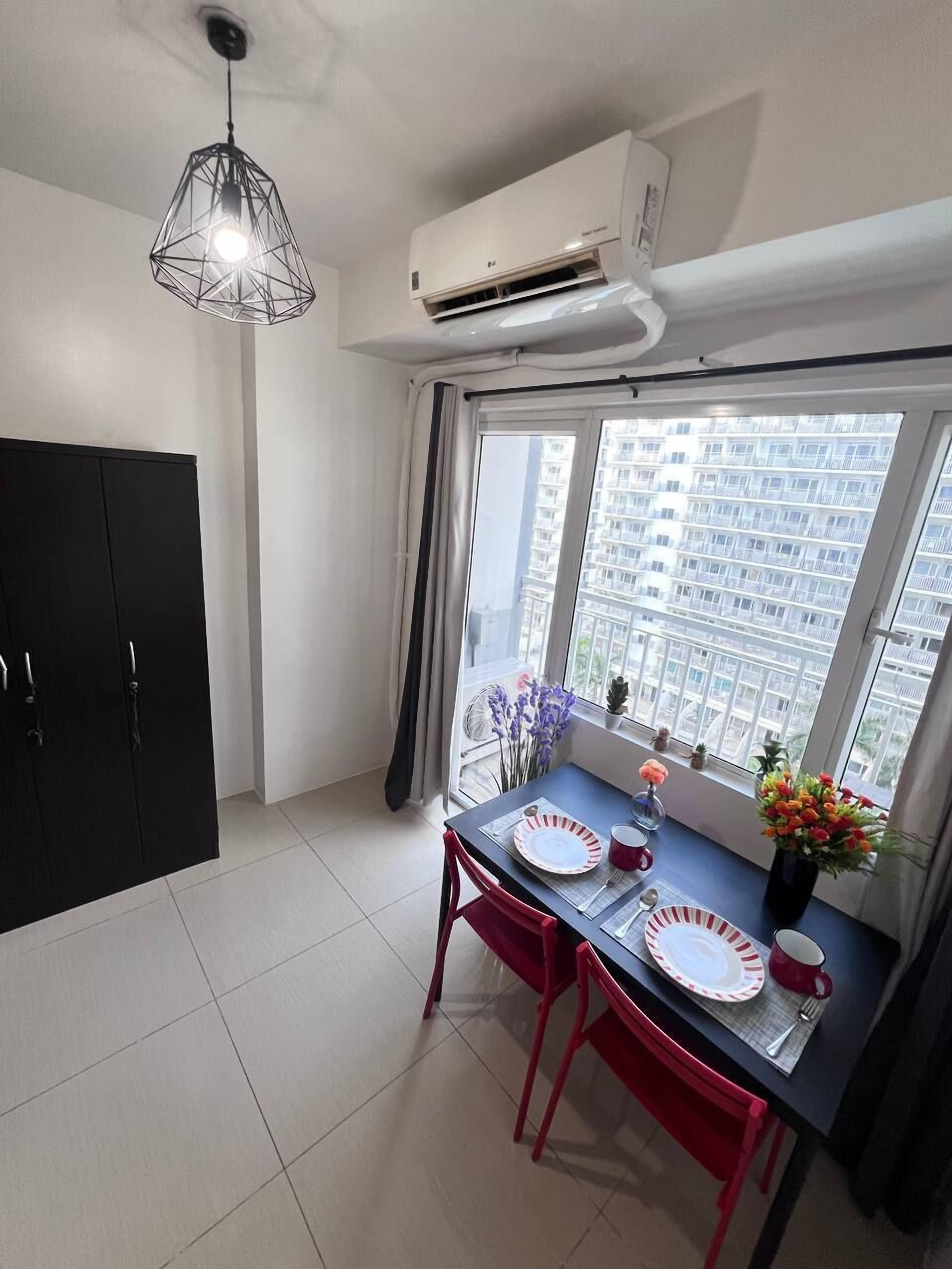 Uma zona de refeições moderna com uma mesa posta para dois, um guarda-roupa preto e um aparelho de ar condicionado sobre a janela.