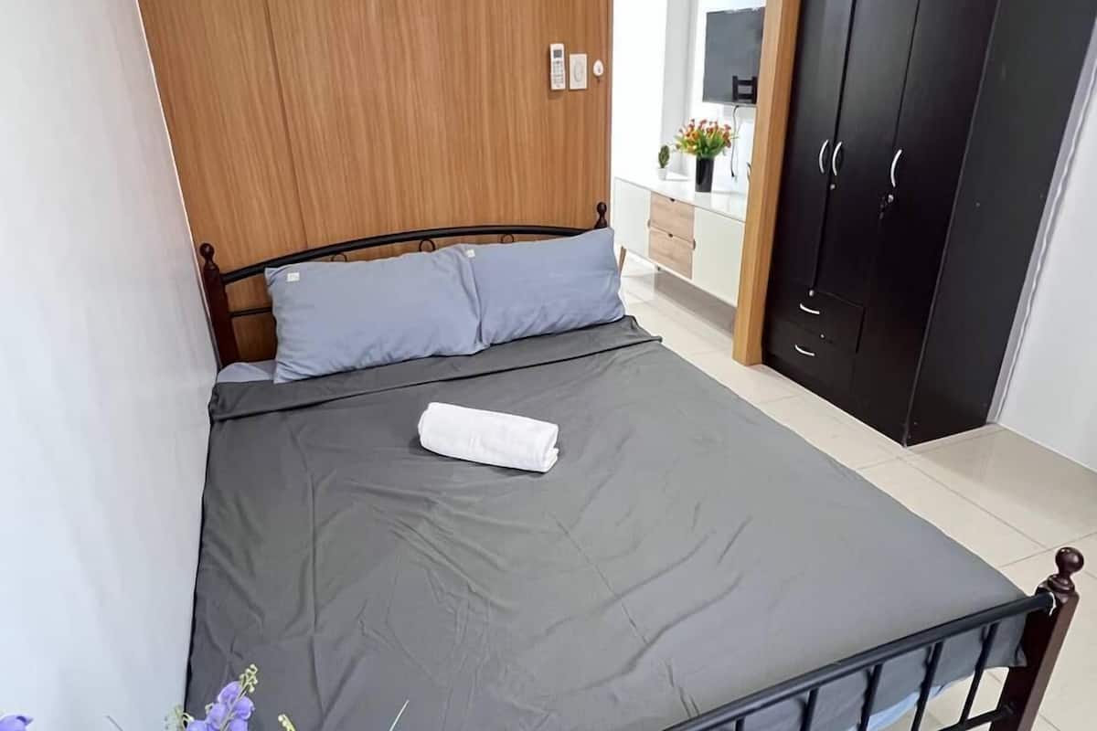 A bedroom with a bed, a wooden headboard, a wardrobe, and a bathroom visible in the background.