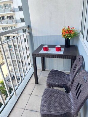 A balcony with a wicker table, two red mugs, and a vase with flowers. - 1 BR Shell Residences Facing amenities (Pasay)