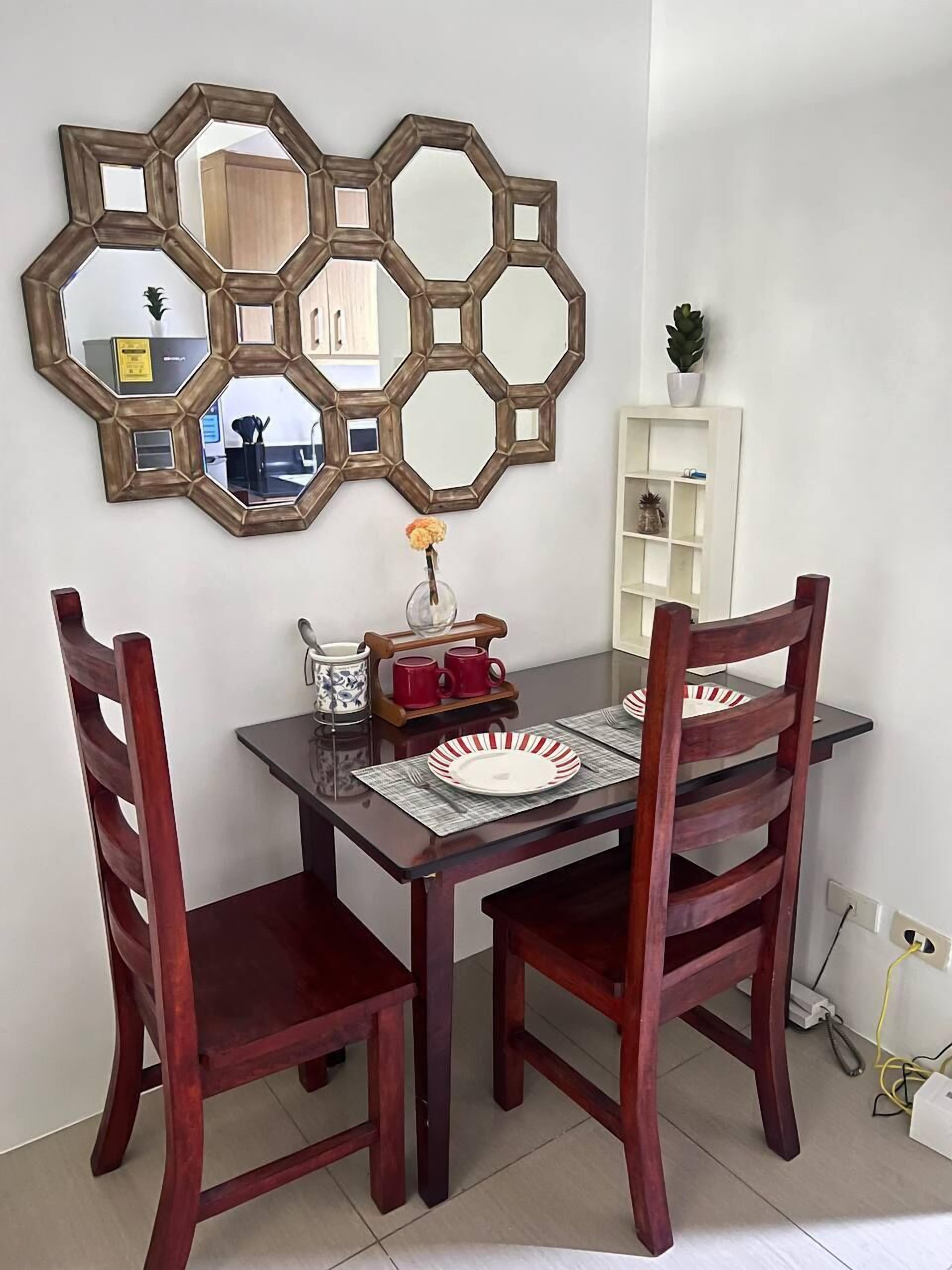 A dining area with a wooden table, two chairs, a decorative mirror, and a small potted plant.