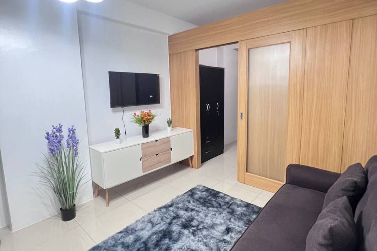 Ein modernes Wohnzimmer mit Sofa, Fernseher, Holzschrank und einer Deckenleuchte.