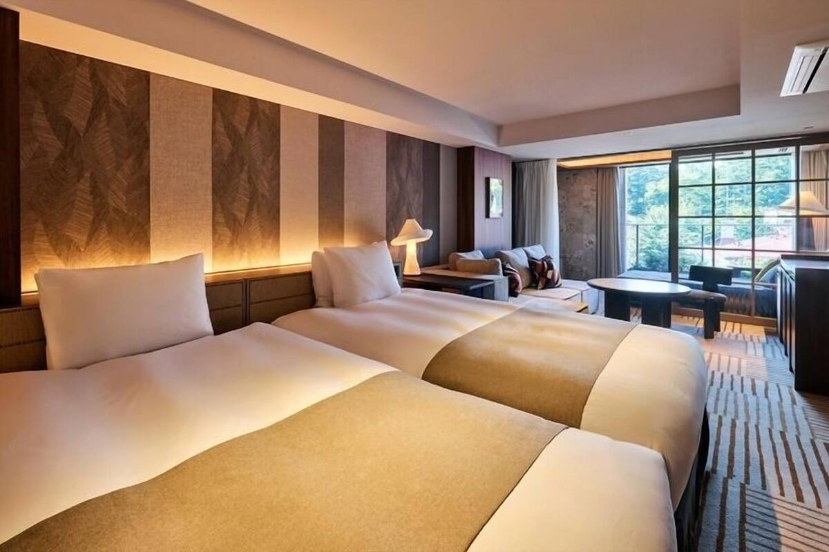 Ein Hotelzimmer mit zwei grossen Betten, einem kleinen Tisch, einer Couch und einem grossen Fenster mit Blick.