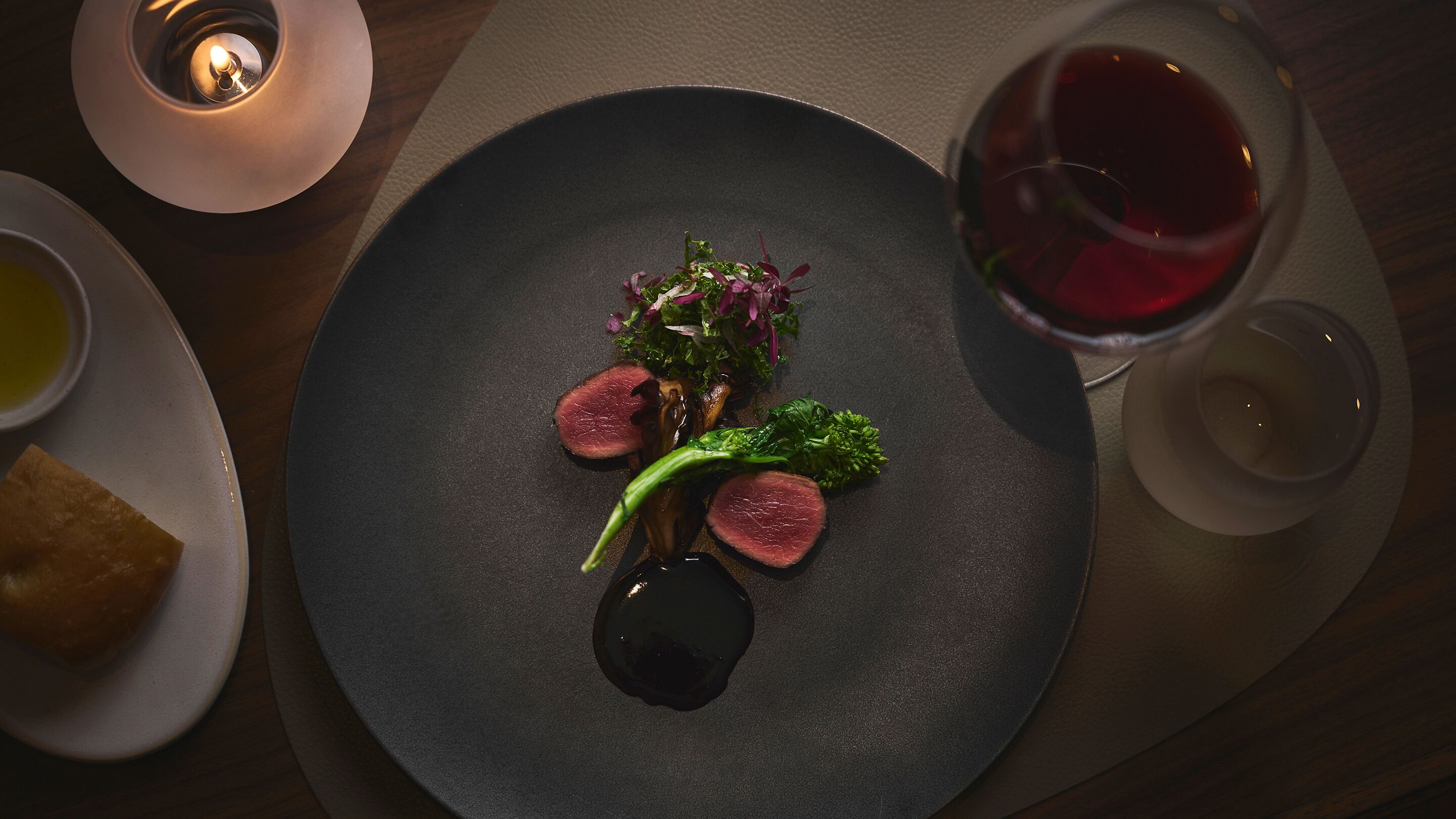 A dining table with a plate of food, a glass of red wine, and a candle.