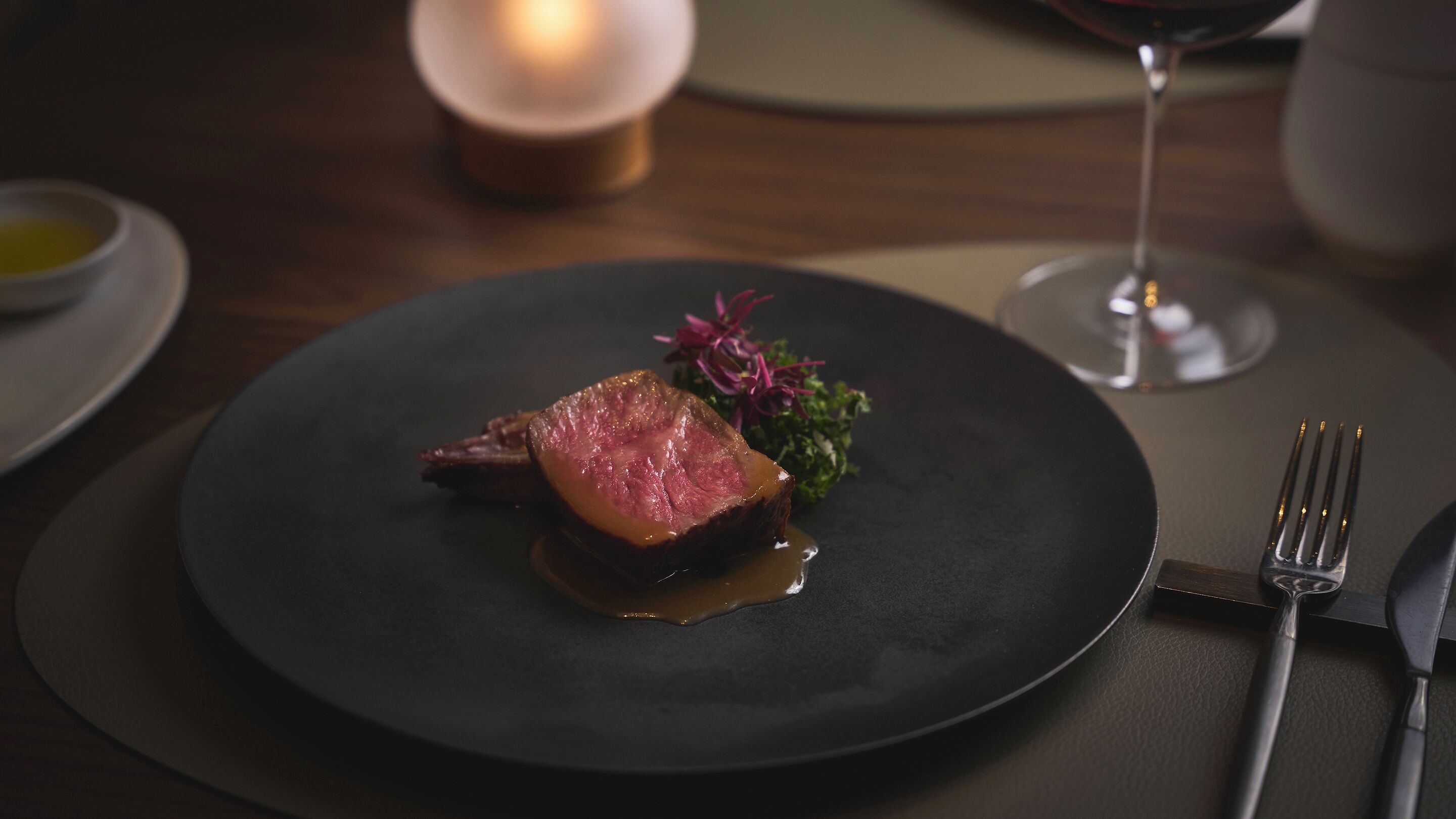 Un plato con carne, una copa de vino tinto y una vela sobre una mesa.