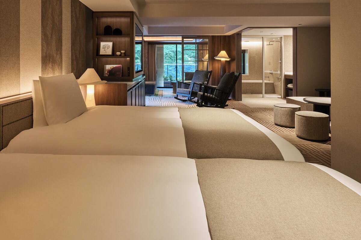 Ein Hotelzimmer mit einem großen Bett, einem Schreibtisch, einem Stuhl und einem kleinen Tisch. Es gibt einen Blick auf einen Balkon und einen Duschbereich.