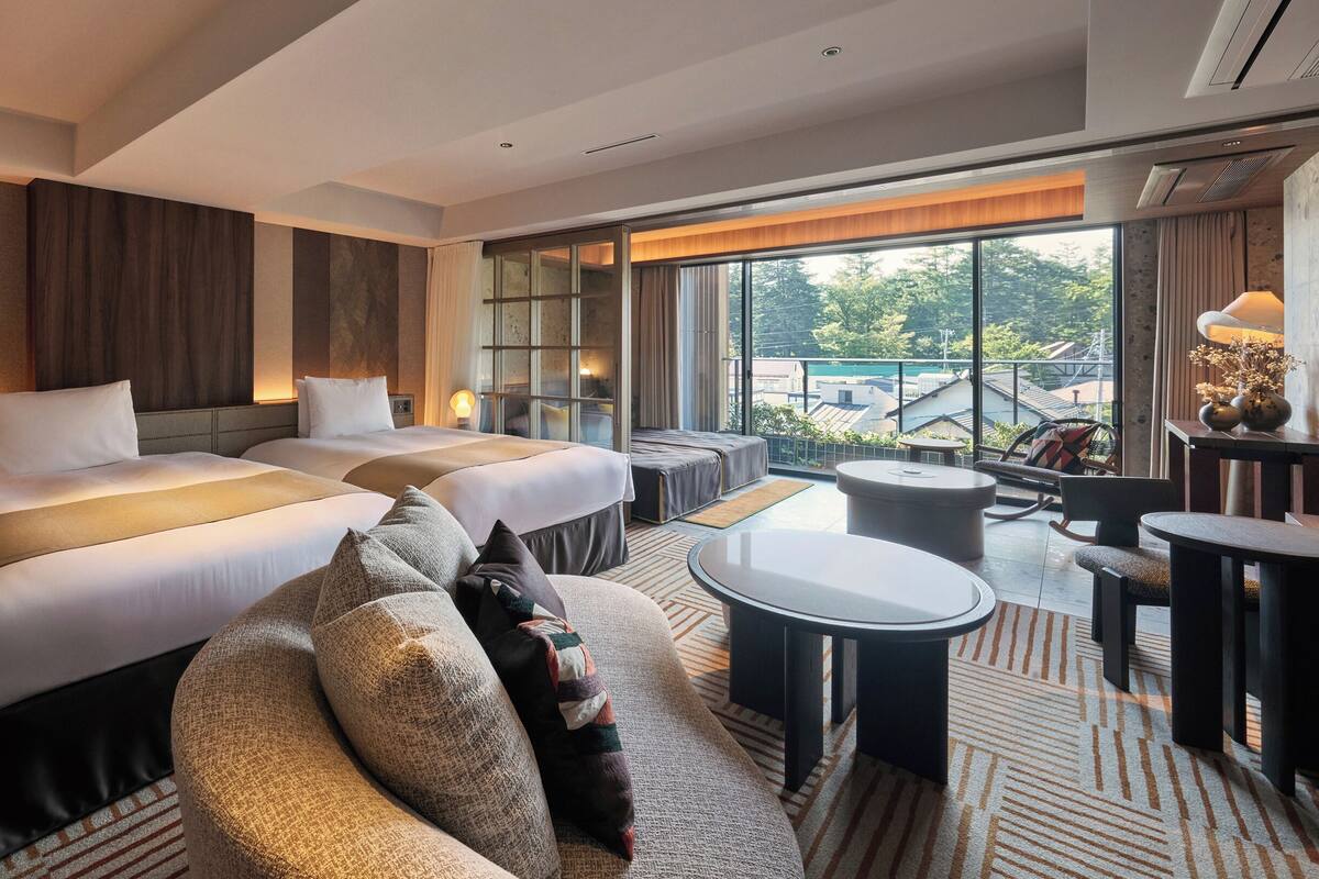 Ein Hotelzimmer mit zwei Betten, einem Schlafsofa, einem kleinen Tisch und Blick ins Freie.
