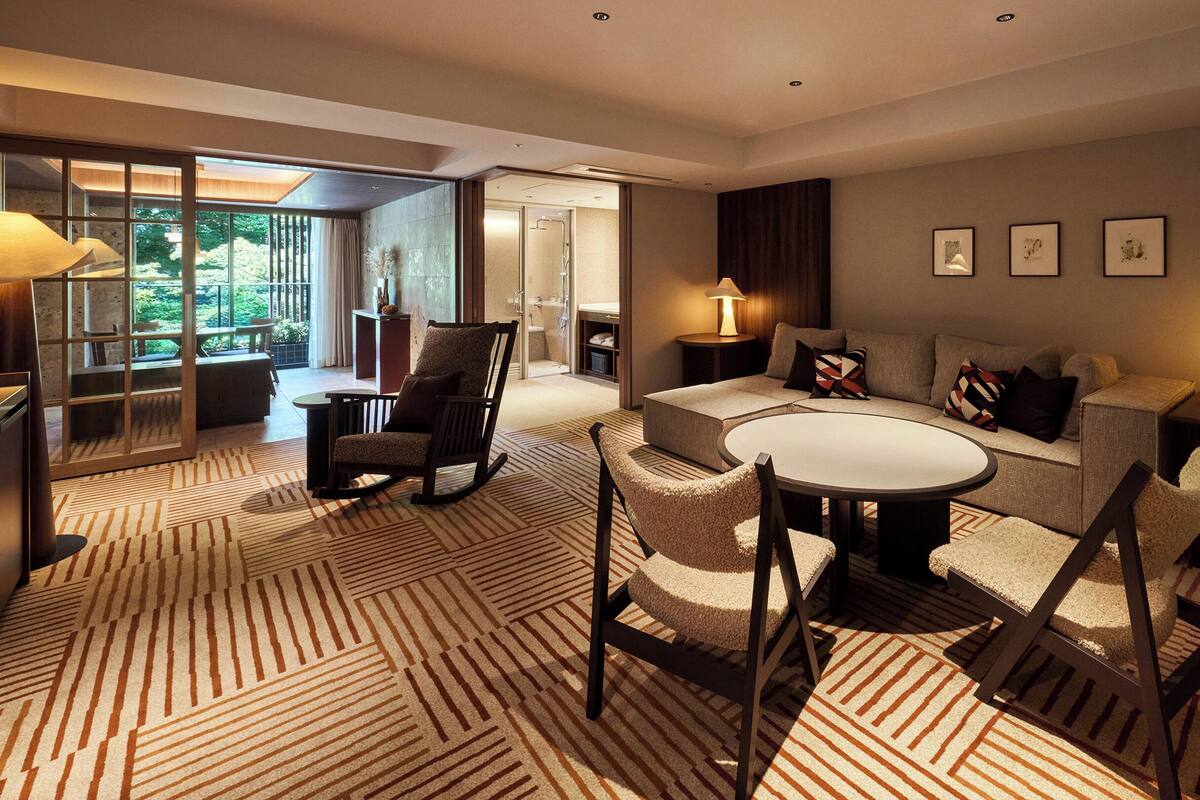Ein modernes Hotelzimmer mit einer Couch, Stühlen, einem Esstisch und Blick ins Freie.
