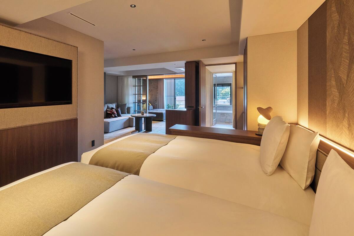A hotel room with a large bed, a TV mounted on the wall, a seating area with a sofa and a small table, and a view of the outdoors through a glass door.