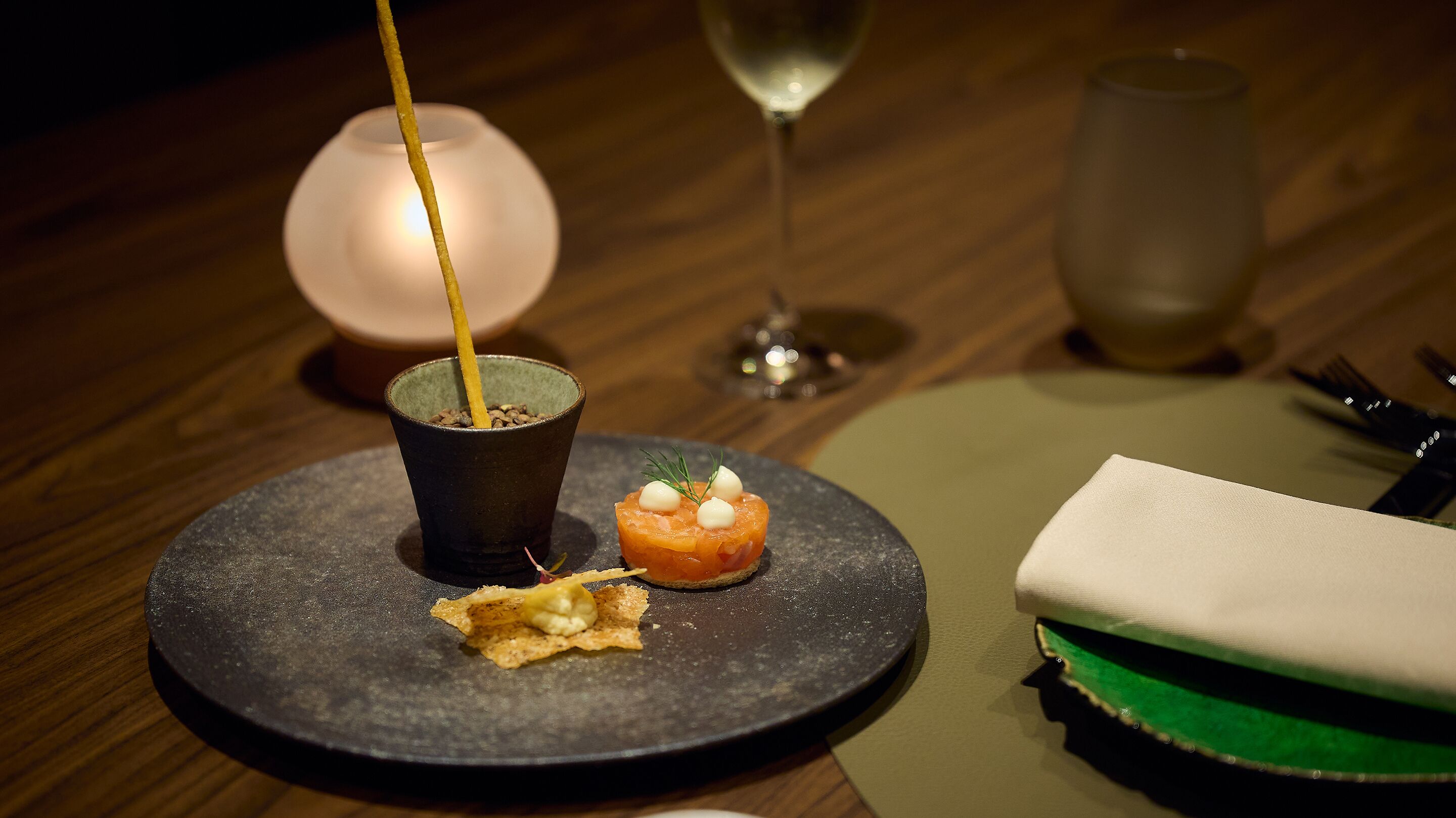 Une table à manger avec une bougie, un verre d’eau et une assiette de nourriture.