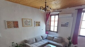 Ett vardagsrum med ett träpanelat tak, en soffa, en fåtölj, ett soffbord och en tv. På väggen hänger tre inramade tavlor och det finns ett fönster med gardiner.