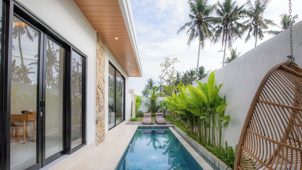 A modern pool area with a glass-enclosed room, a stone wall, and lush greenery. - Villa Sardegna Ubud (Ubud)
