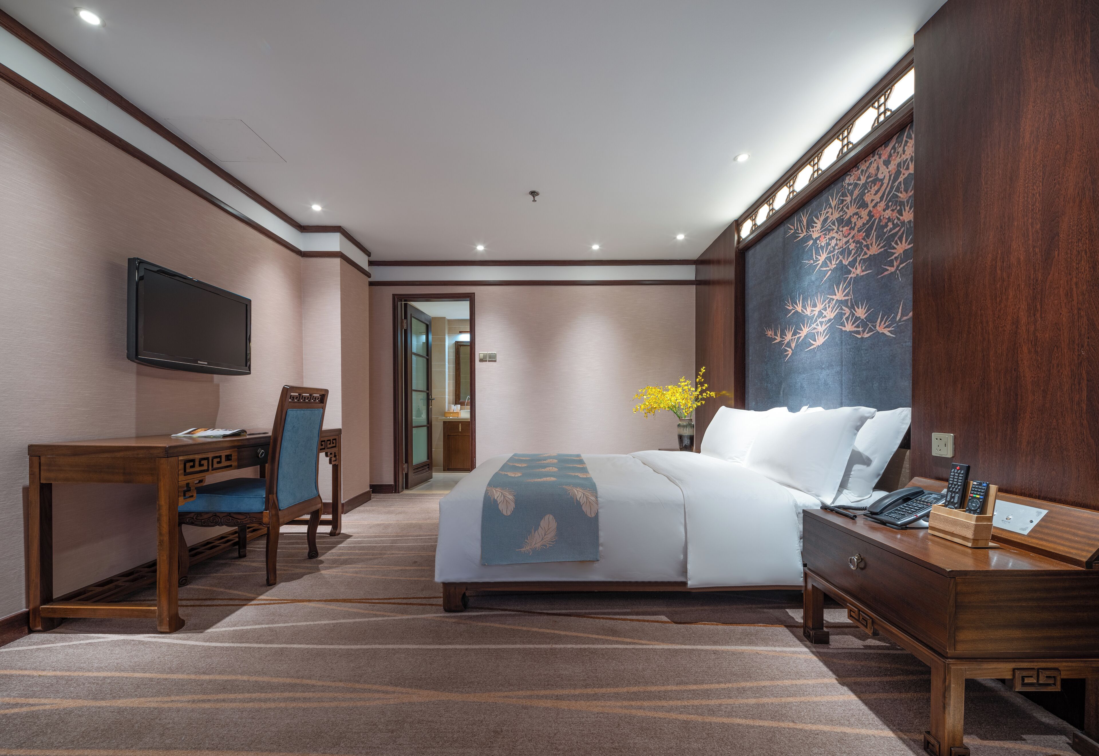 A hotel room with a bed, a desk, a chair, a TV, and a large artwork on the wall.