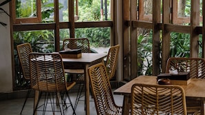 A dining area with wicker chairs and tables, large windows with a view of greenery. - Lakubumi Pavilion (Ungasan)