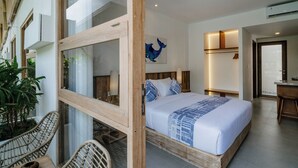 A modern hotel room with a large bed, a wooden-framed window, a dining area with wicker chairs, and a view of the street. - Lakubumi Pavilion (Ungasan)